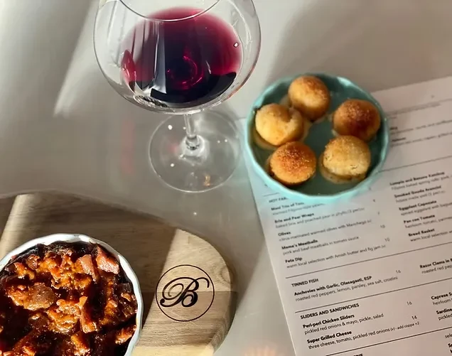 Restaurant table with red wine, spherical appetizers, chunky stew, and menu.