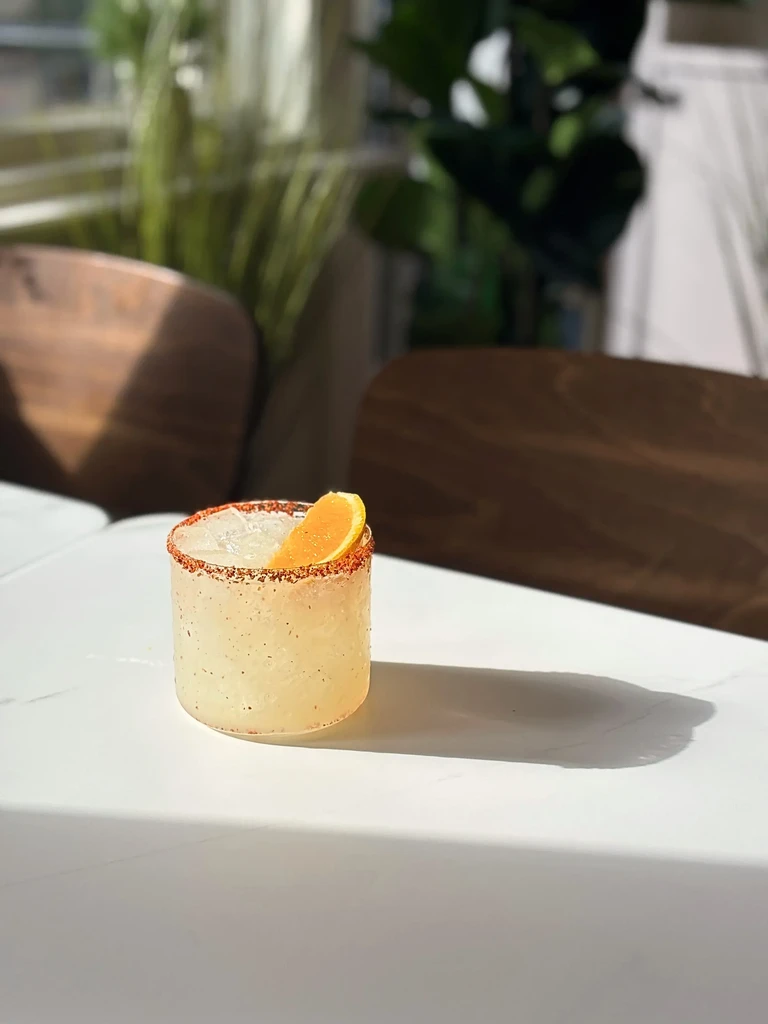 Spiced rim cocktail with orange wedge on white table.