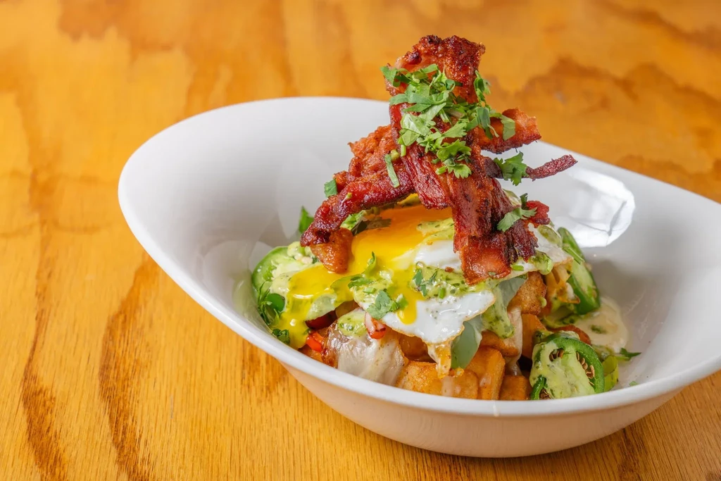 Breakfast bowl with crispy bacon, runny fried egg, and green-sauced vegetables.