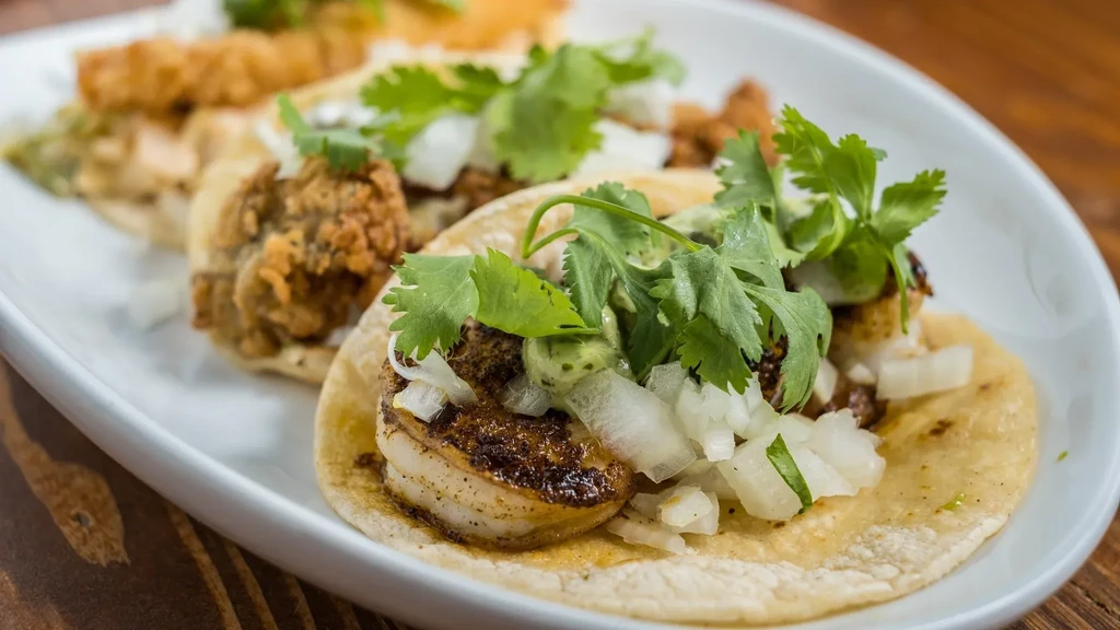 Two grilled seafood tacos with cilantro, onions, and green sauce.