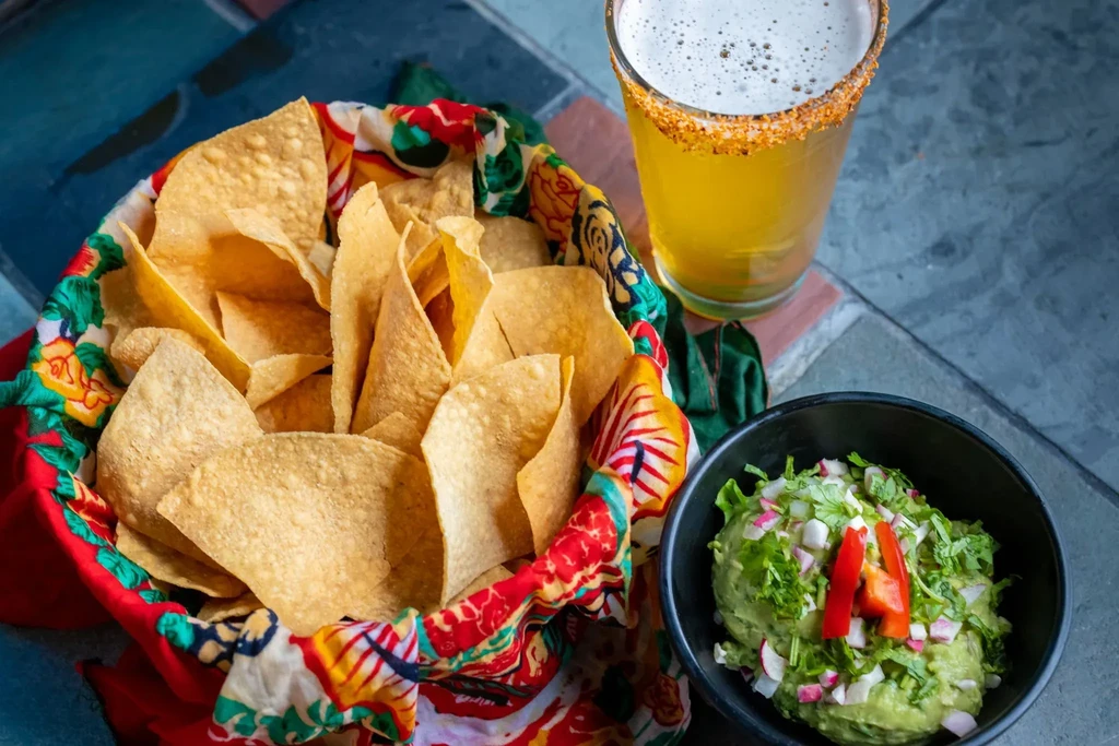 Overflowing basket of tortilla chips, guacamole, and beer with a salt rim.