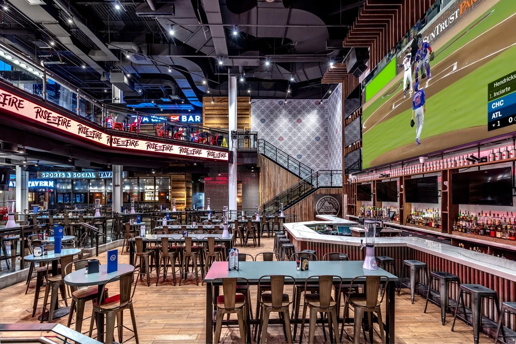 Multi-level industrial sports bar with large screen showing baseball.