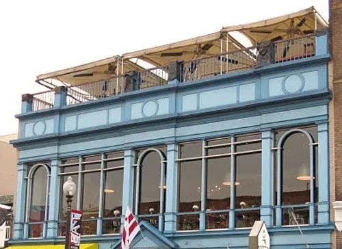 Light blue building with arched windows and a rooftop patio with light-colored awnings.