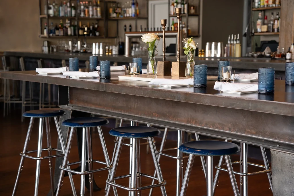 Rustic-industrial counter with blue bar stools and place settings in a modern bar.
