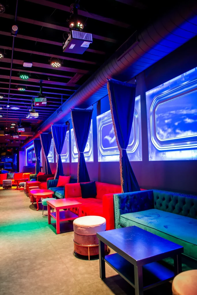 Empty, modern lounge with colorful lighting, velvet booths, and illuminated sky panels.