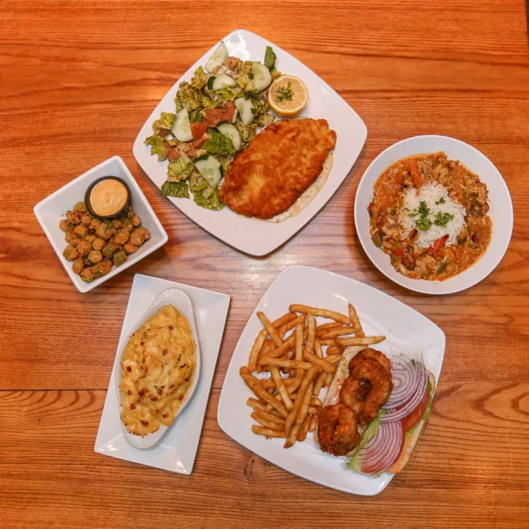 Overhead shot of diverse restaurant dishes on a warm wooden table.
