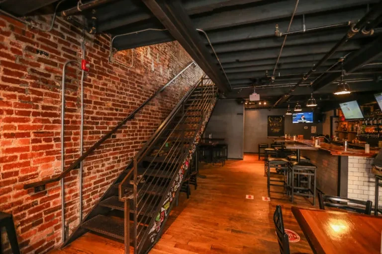 Industrial restaurant interior featuring a metal staircase, exposed brick, and bar.