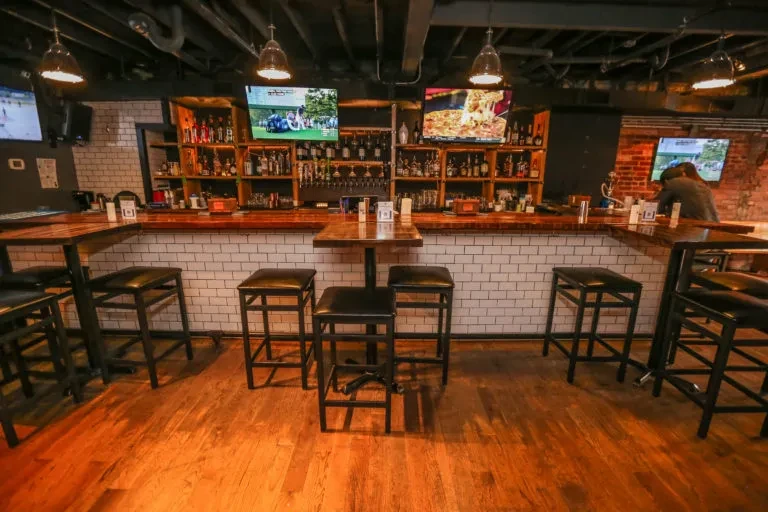 Modern bar's U-shaped counter, liquor shelves, beer taps, and televisions.