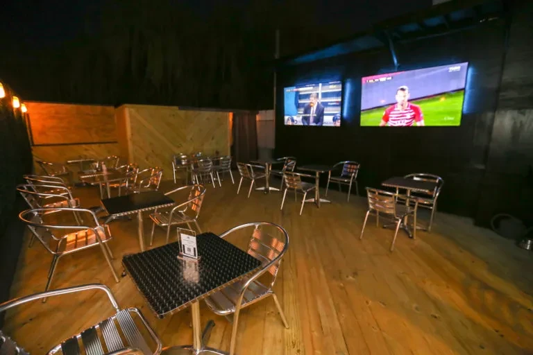 Empty, dimly lit restaurant patio with metallic seating and two sports TVs.