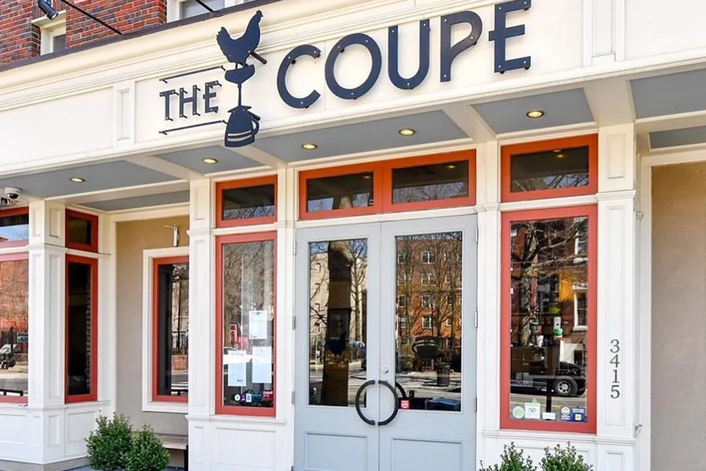 Exterior of The Coupe restaurant: brick, red-framed windows, chicken logo.