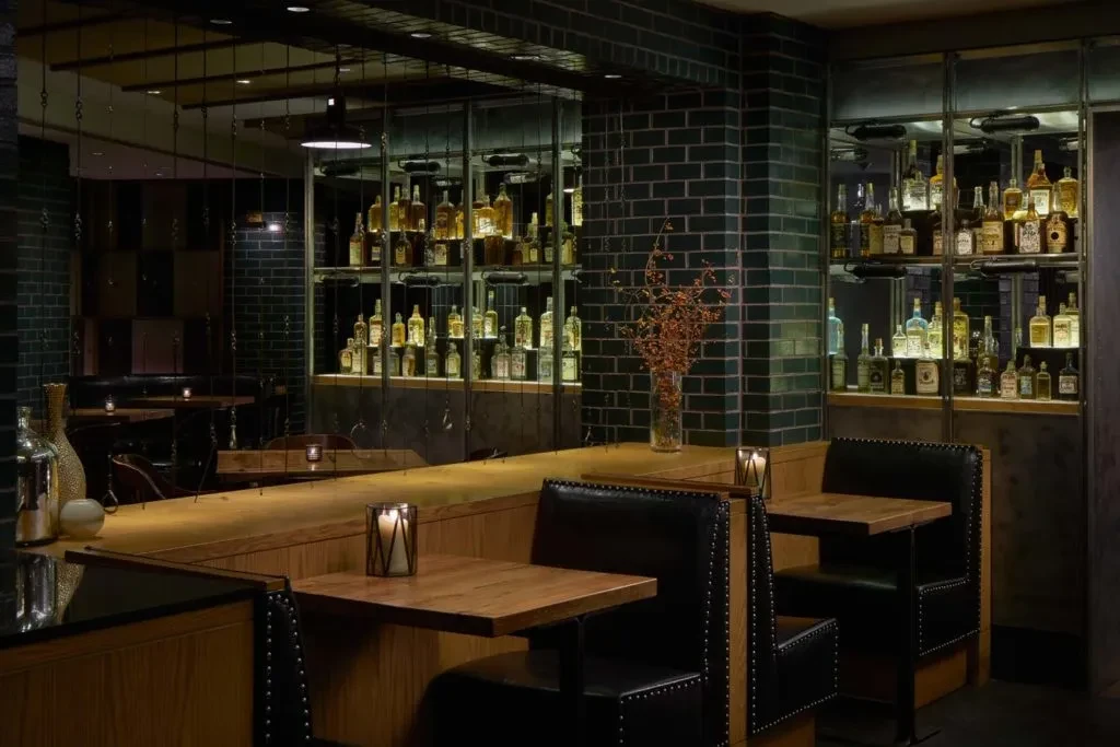 Dimly lit restaurant interior with empty tables, candles, and backlit bar.