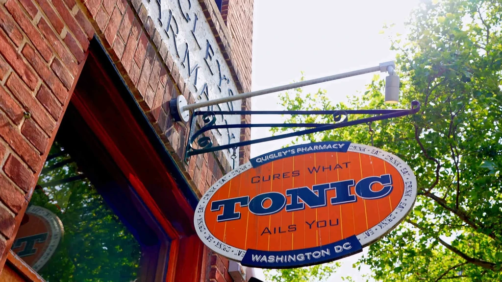 Oval orange Tonic Quigley's Pharmacy sign on a red brick building.