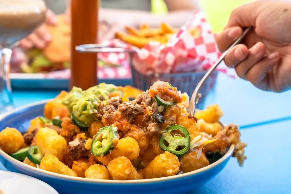 Hand scooping loaded tater tots with meat, guacamole, and cheese.