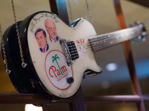 White electric guitar with caricatures, signatures, and Palm Restaurant logo.