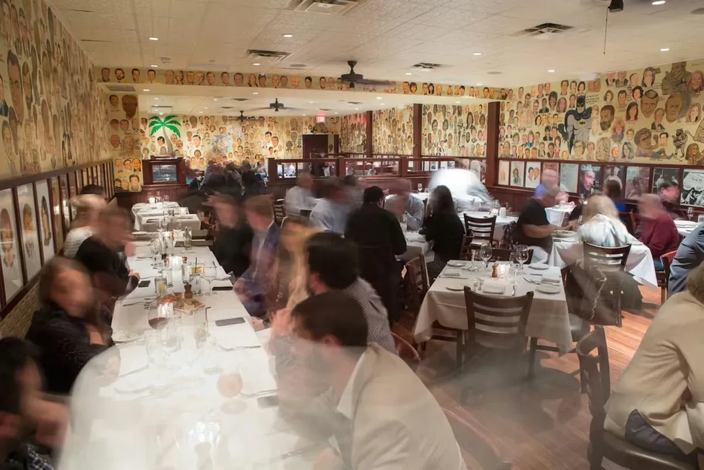 Bustling restaurant dining room with blurred patrons and caricature walls.