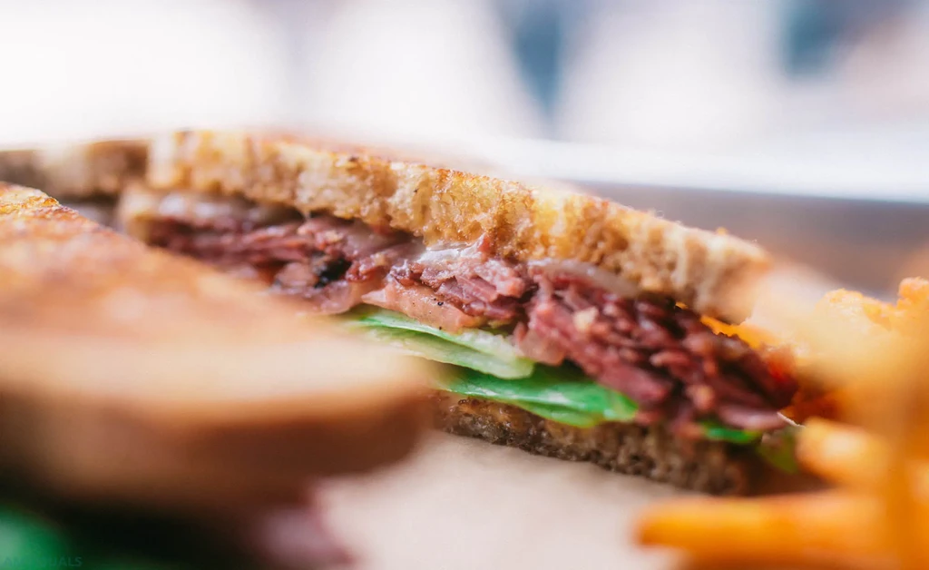 Cut toasted sandwich with meat, melted cheese, lettuce, and fries.