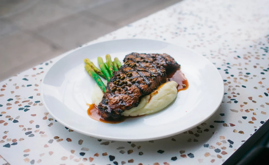 Peppercorn steak with mashed potatoes, asparagus, and rich sauce.