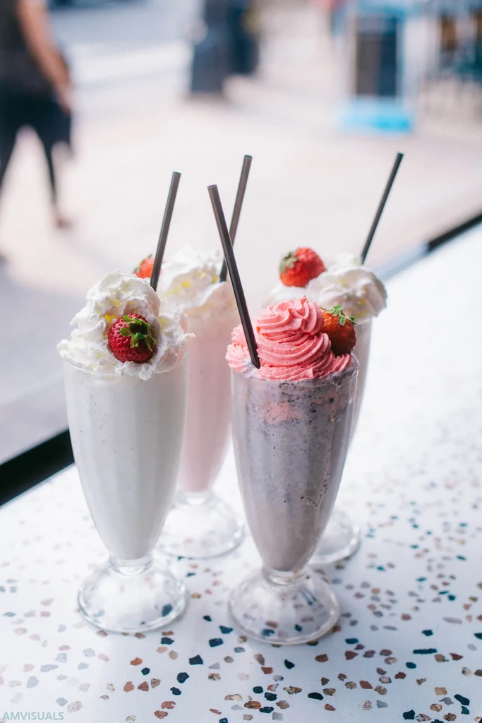 Four colorful milkshakes with whipped cream and strawberries on a table.