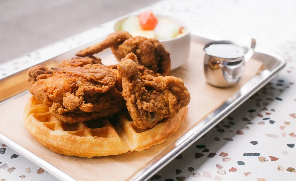 Chicken and waffles with fruit salad and syrup on a metal tray.