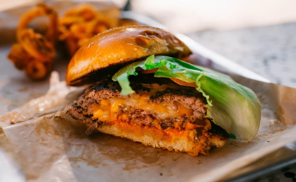 Halved burger with patty, melted cheese, lettuce, sauce, and curly fries.