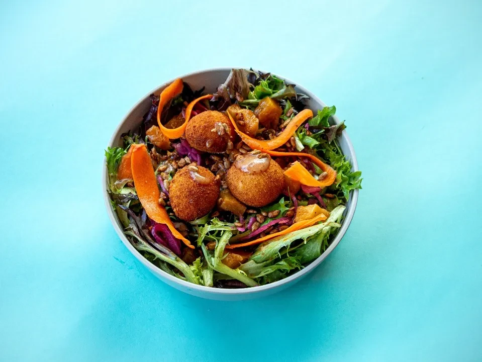 Colorful salad with breaded spheres, mixed greens, carrots, and roasted vegetables.
