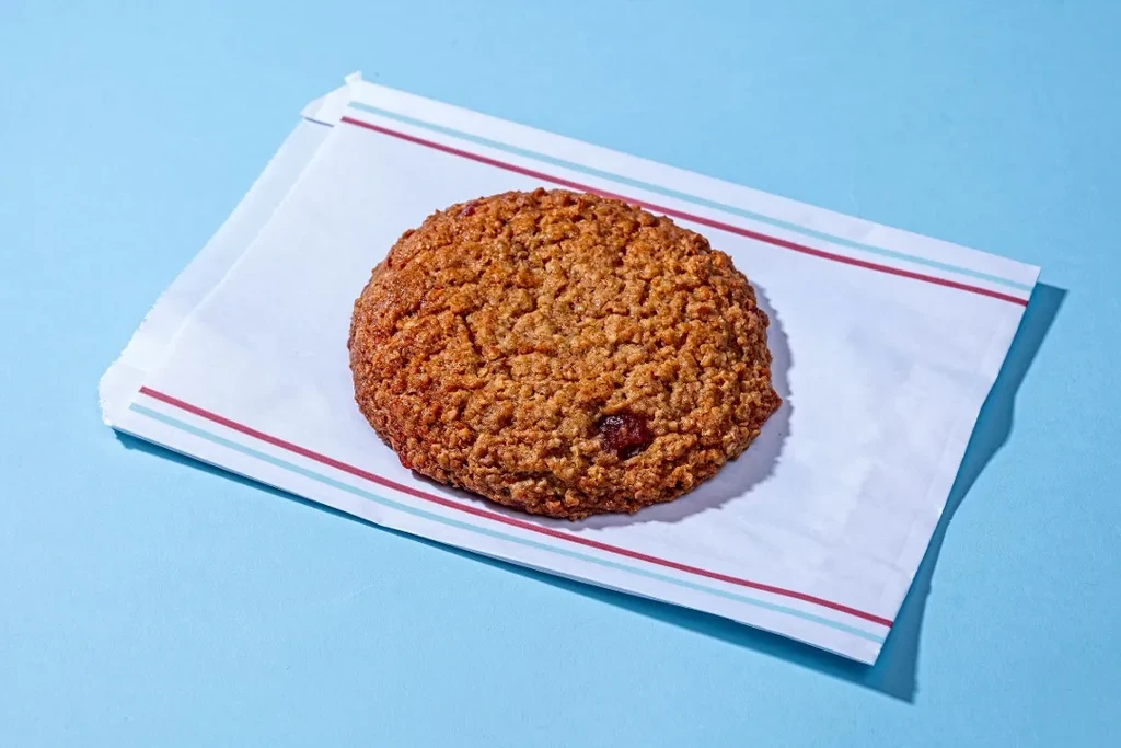 Round oatmeal cookie with dried fruit on striped paper, blue background.