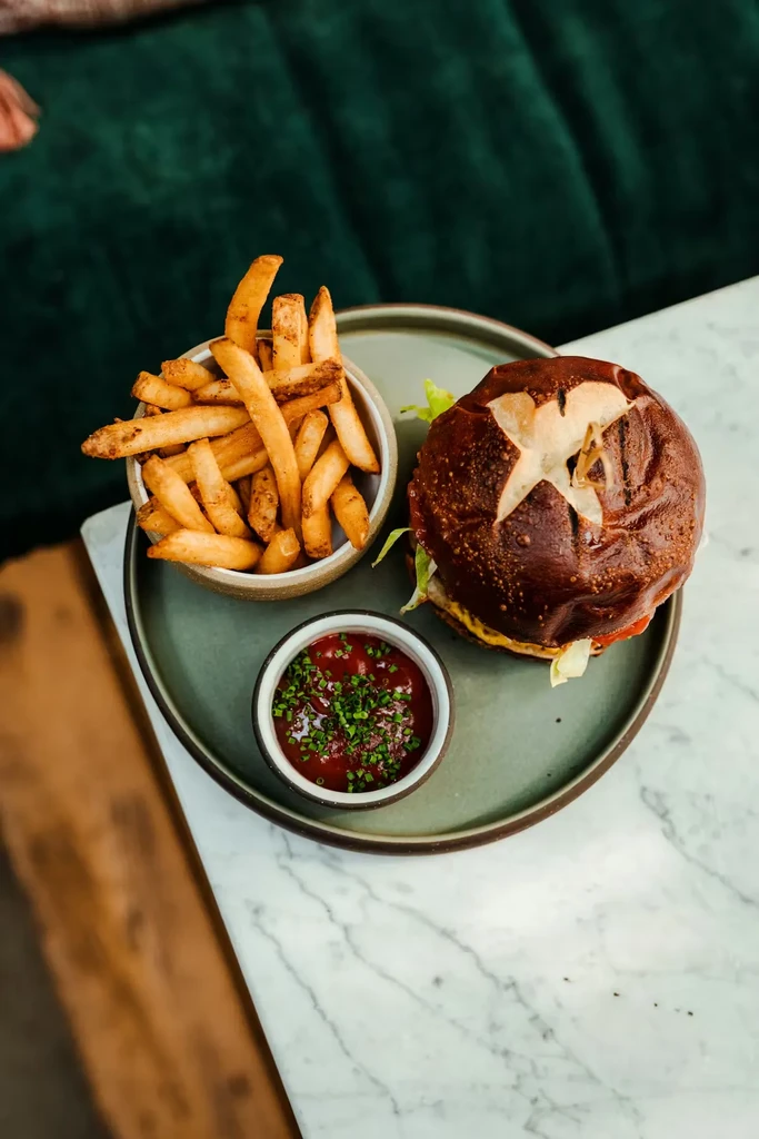 Burger with pretzel bun, fries, and chive ketchup, top-down view.