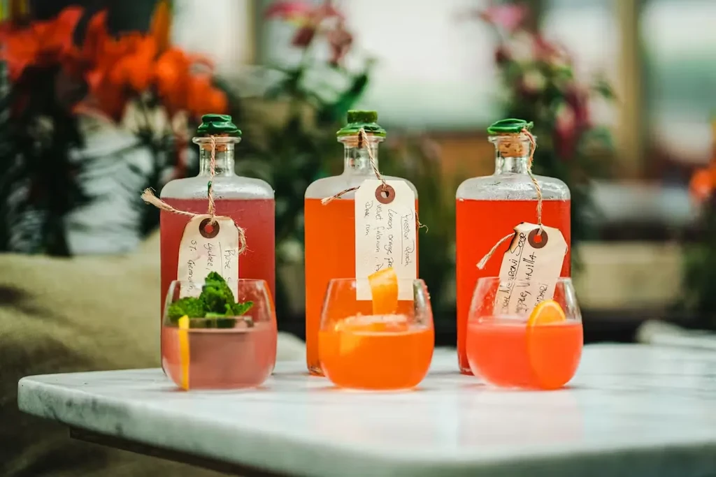 Three colorful bottled beverages with handwritten descriptive tags and garnishes.