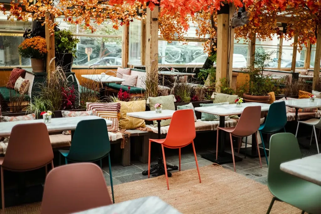Restaurant dining area with autumn leaves, colorful chairs, and plants.