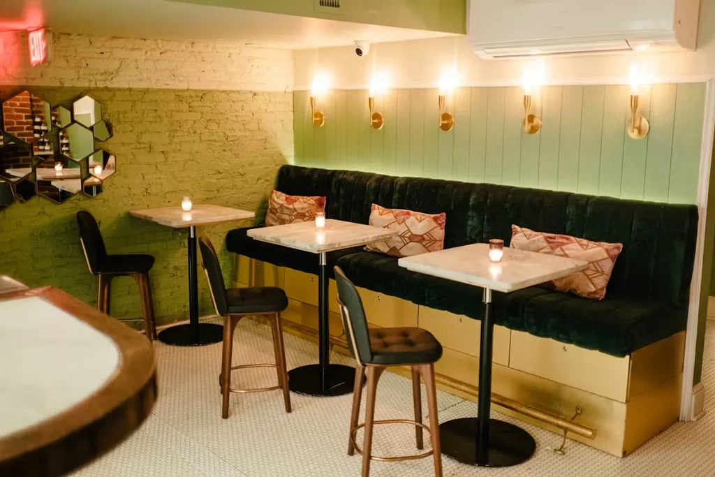 Restaurant with green velvet banquette, white marble tables, and mosaic floor.