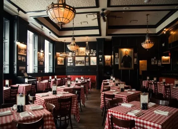 Dark traditional restaurant with red checkered tables, gallery walls, and chandeliers.