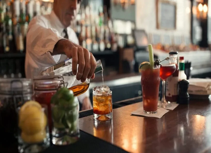 Bartender pouring a drink behind a well-stocked bar.