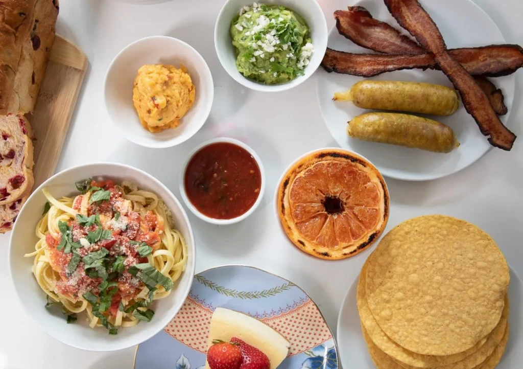 Overhead shot of a diverse meal featuring pasta, meats, dips, and dessert.