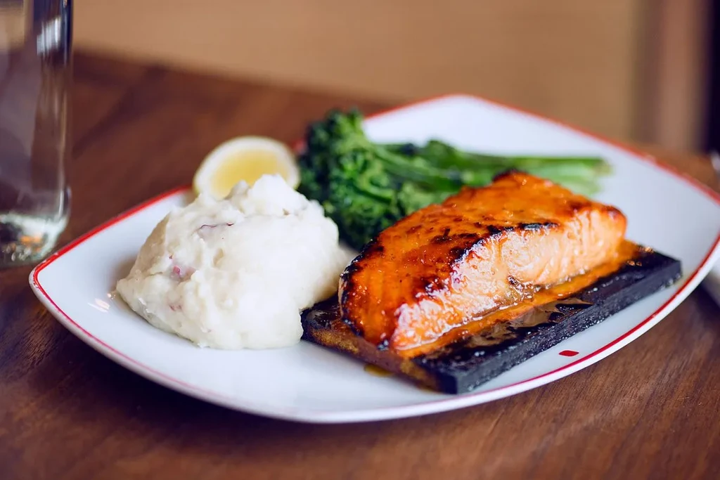 Grilled salmon with mashed potatoes, green vegetables, and lemon on a plate.