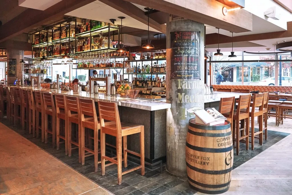 Modern rustic bar area with marble counter, liquor bottles, warm lighting.