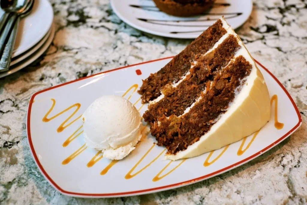 Carrot cake slice with cream cheese frosting, vanilla ice cream, caramel drizzle.
