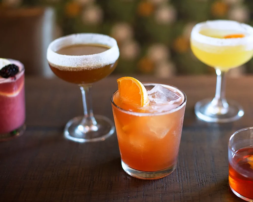 Vibrant, garnished cocktails in various glasses on a wooden table.
