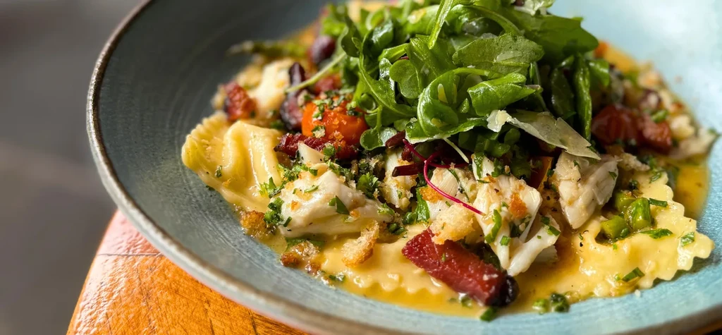 Gourmet pasta in teal bowl with yellow sauce, arugula, cheese, fish.