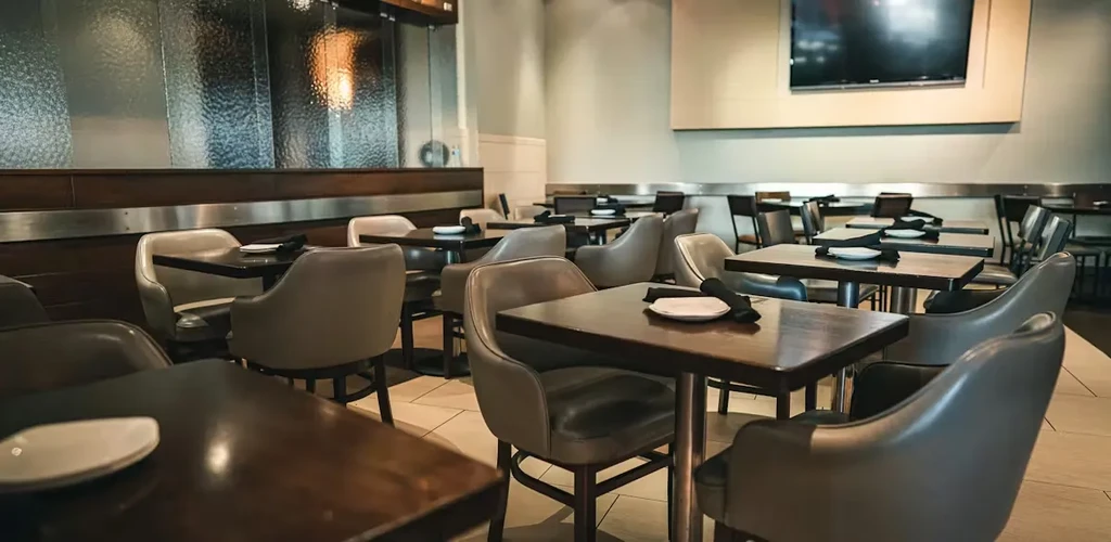 Empty modern restaurant with dark tables, beige chairs, and glass partitions.
