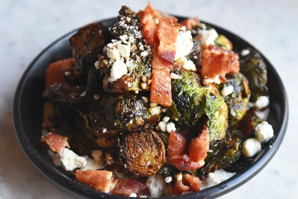 Charred Brussels sprouts with crispy bacon and crumbled cheese in a bowl.