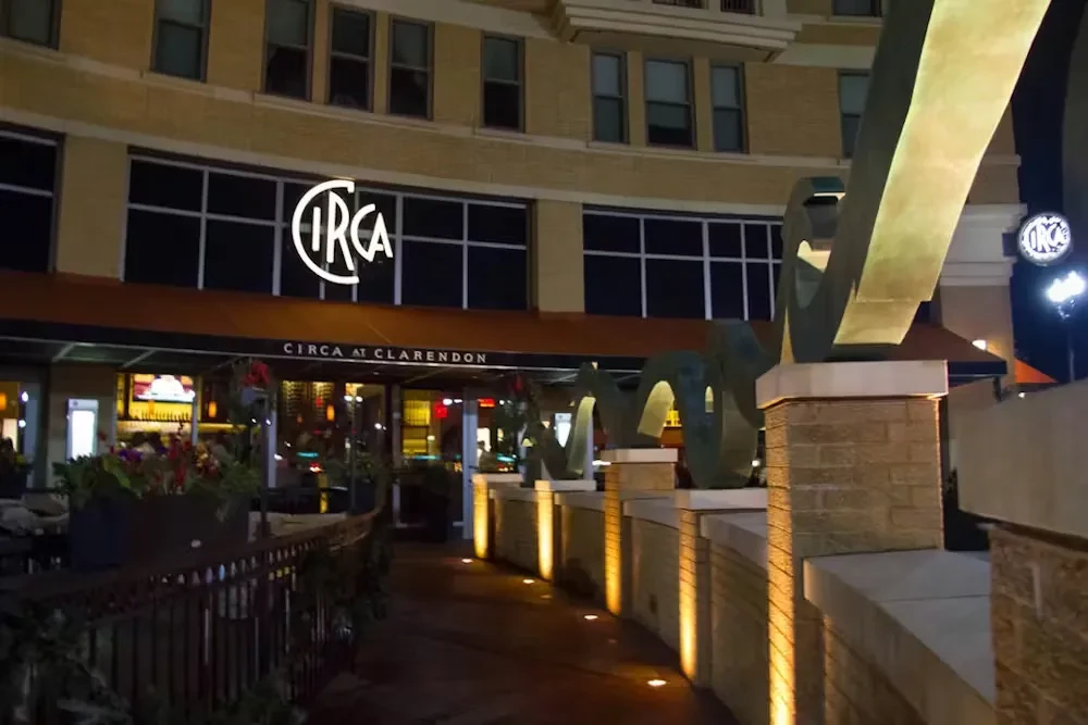Nighttime exterior of CIRCA restaurant with patio and abstract sculpture.