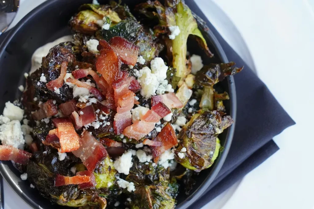 Roasted Brussels sprouts with bacon and white cheese in a black bowl.