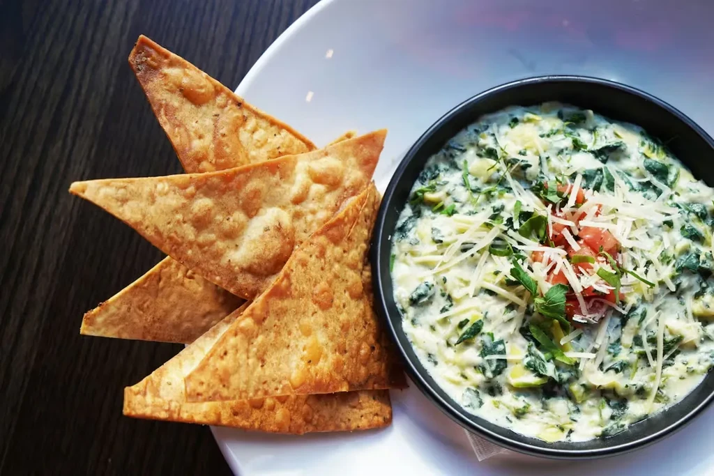 Overhead view: spinach dip with cheese, tomatoes, herbs, tortilla chips.
