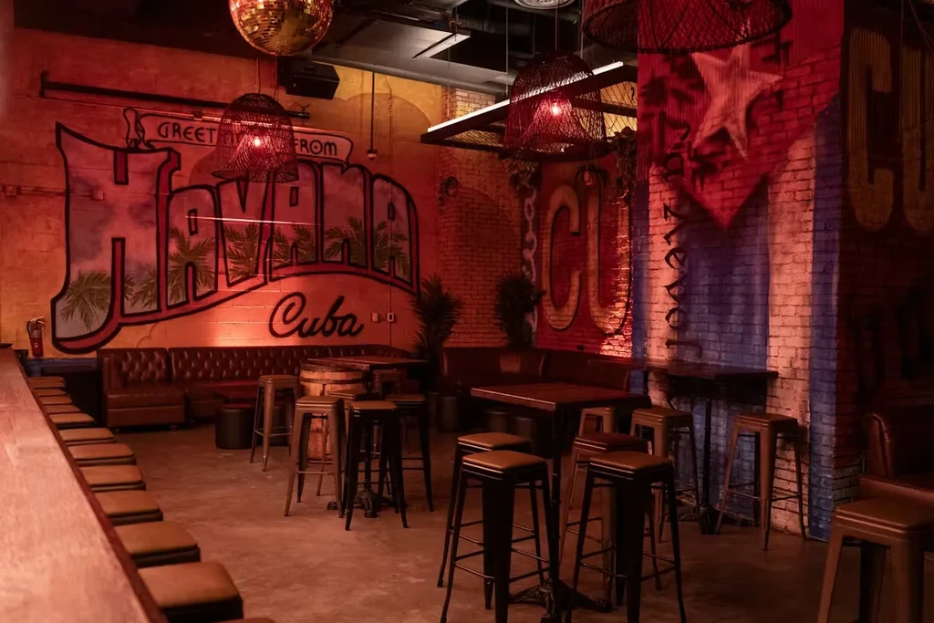 Warmly lit Cuban bar interior with Havana murals and leather seating.