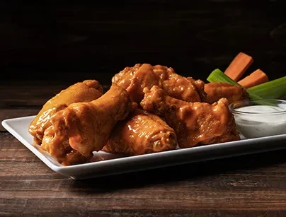 Plate of buffalo chicken wings with dipping sauce, celery, and carrots.