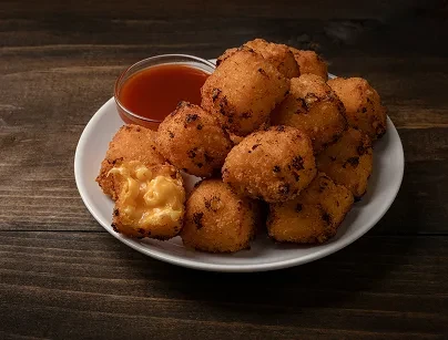Golden-brown fried mac and cheese bites, one broken, with sauce.