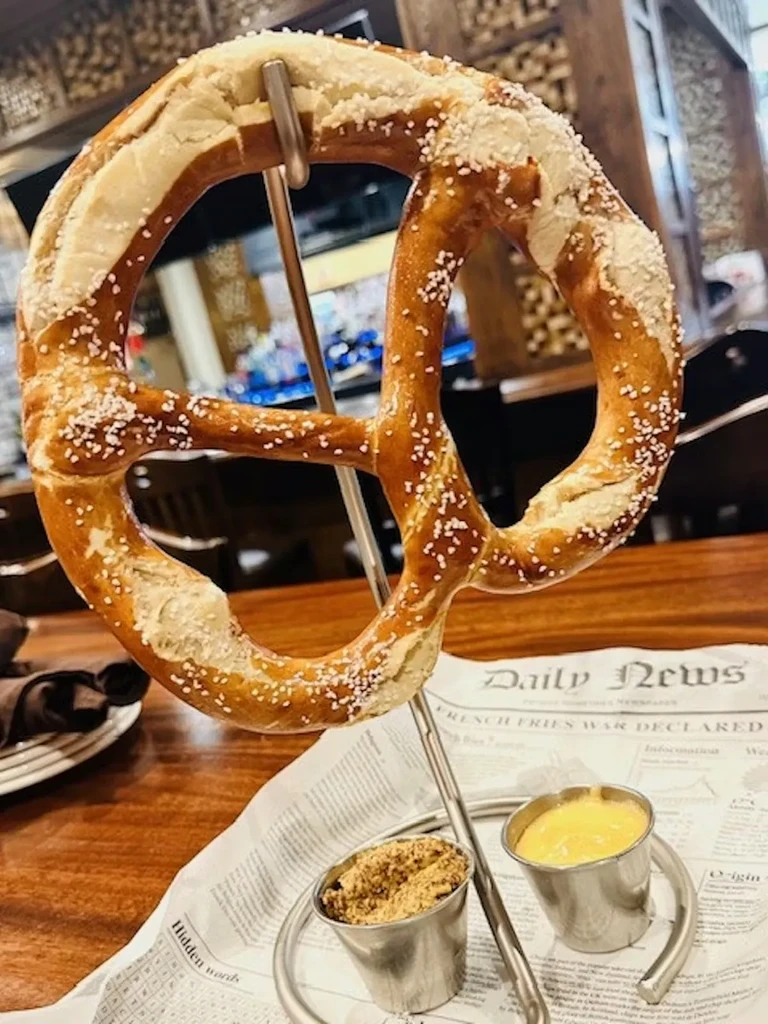 Salted pretzel on a metal stand with two sauces and newspaper placemat.