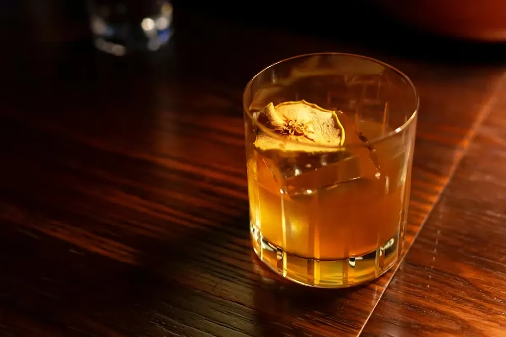 Amber cocktail in faceted rocks glass with ice and dried garnish.