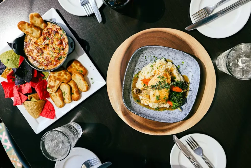 Overhead view of cheesy gratin, colorful chips, roasted chicken, and vegetables.