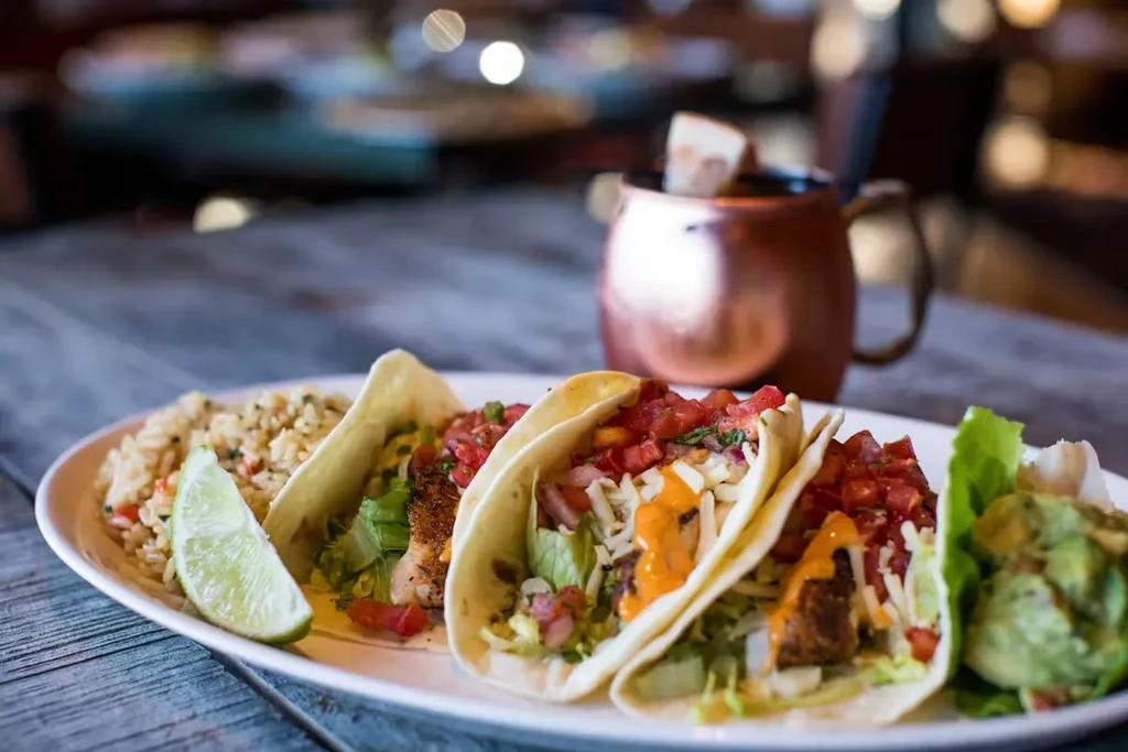 Three loaded fish/chicken tacos, seasoned rice, guacamole on wood.